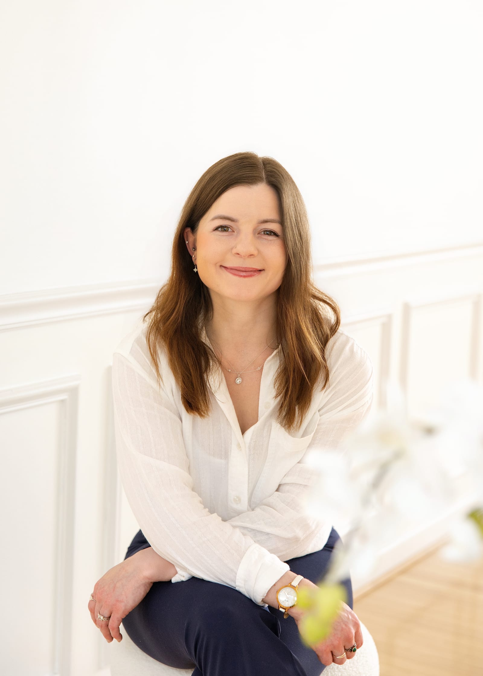 Professional in a white blouse seated on a ledge in a bright panelled room