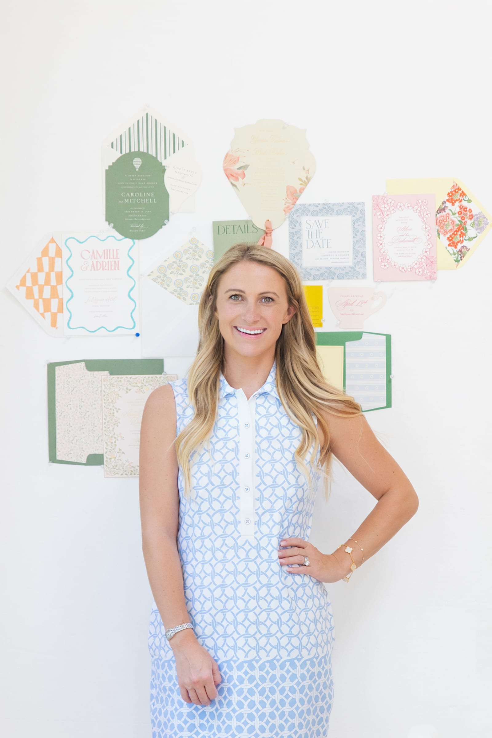 Founder in a patterned blue dress standing in front of a pinboard of design work