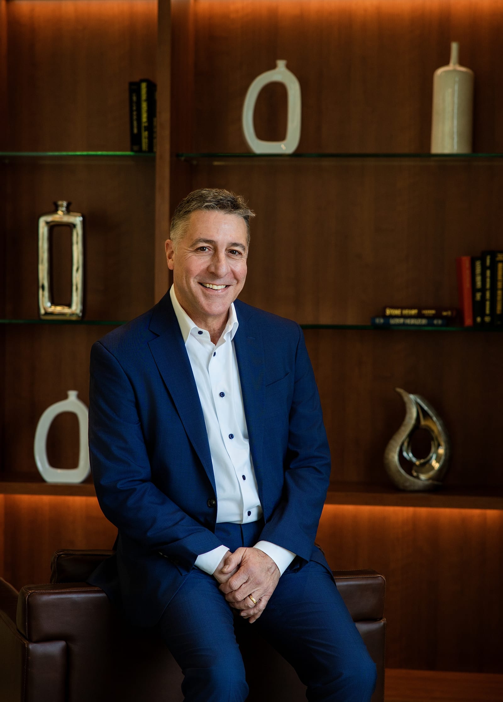 Executive in a navy blazer seated in front of a warmly lit display shelf of ceramics