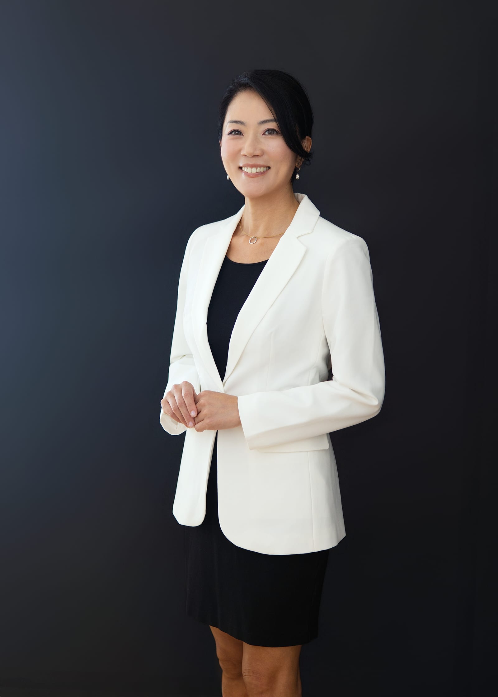 Executive in a white blazer and black dress, arms folded, against a deep charcoal ground