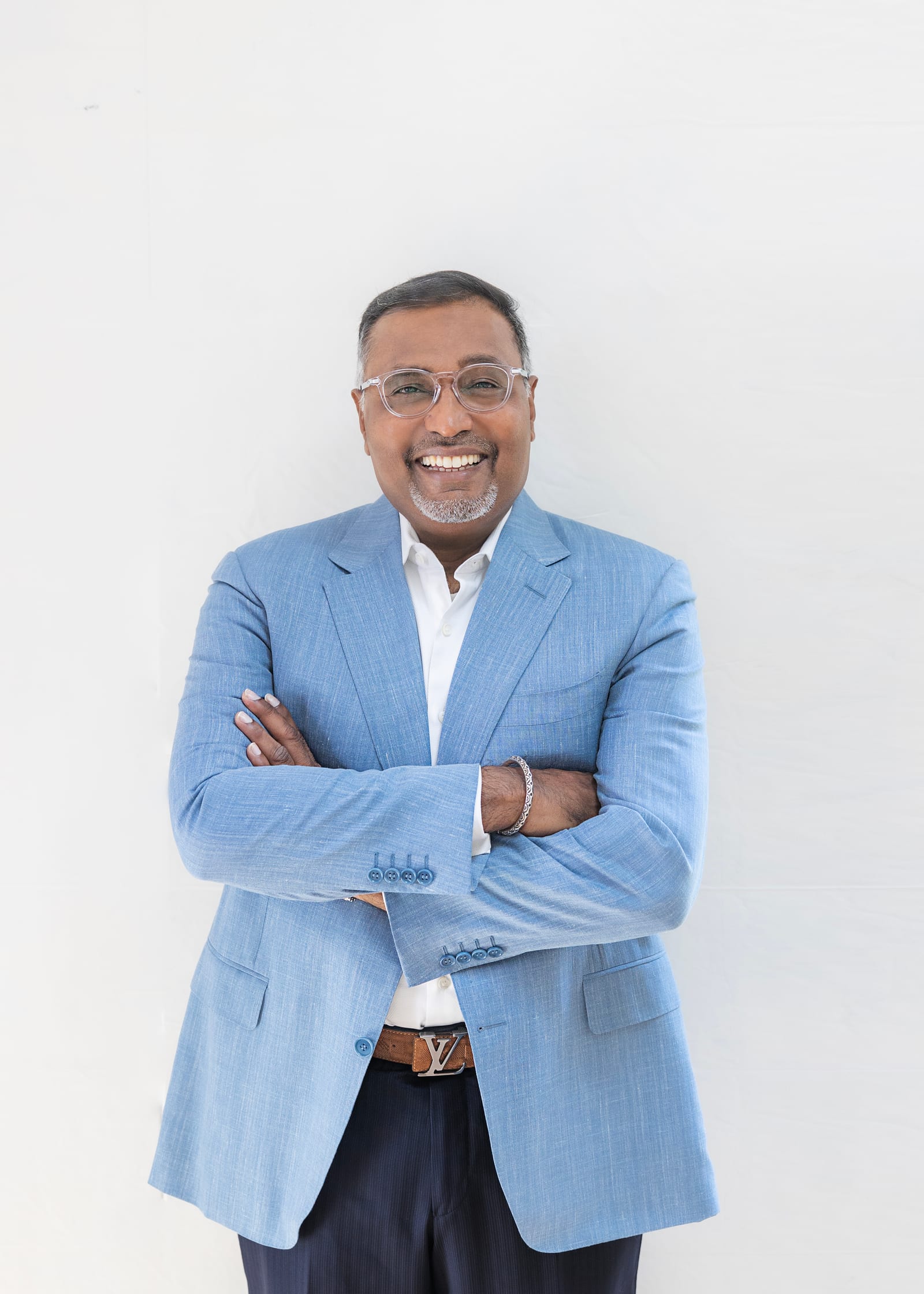 Executive in a light blue blazer and open shirt, arms crossed, against white