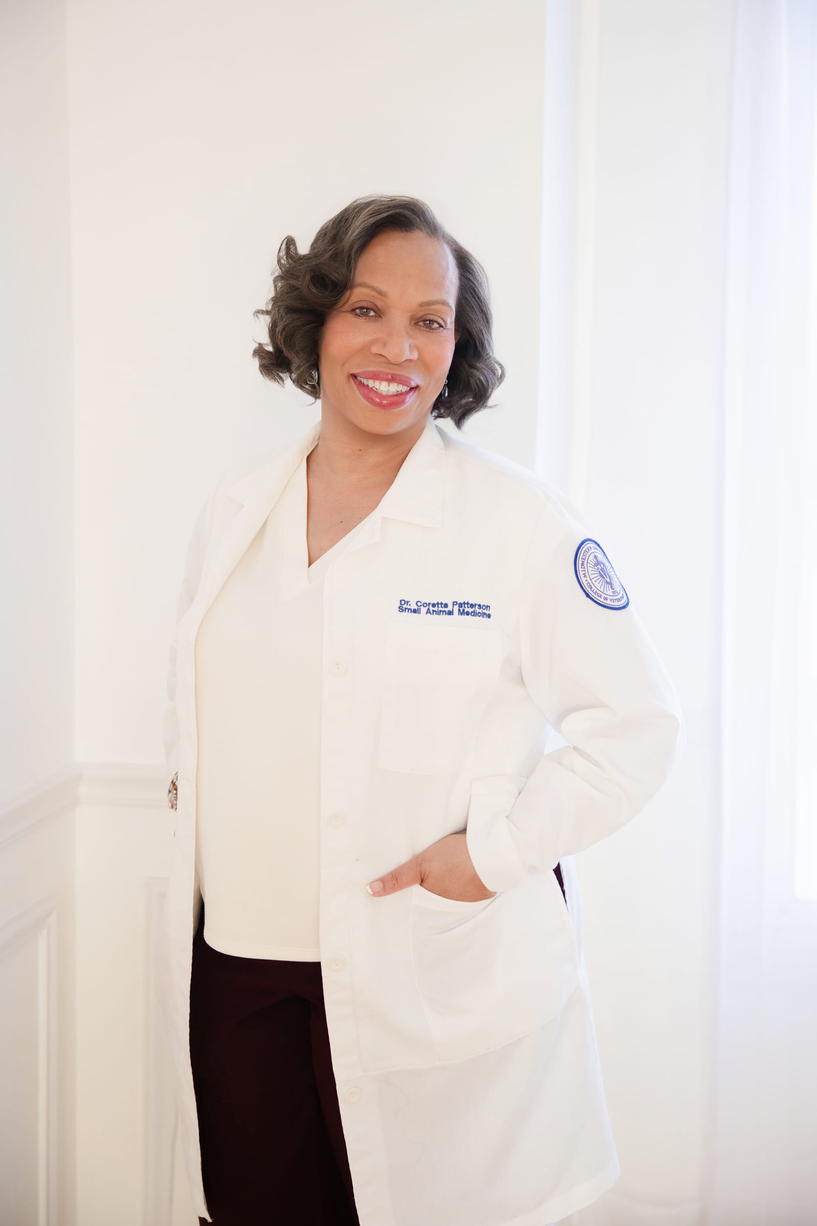 Physician in a white coat standing with hands in pockets against a bright white wall