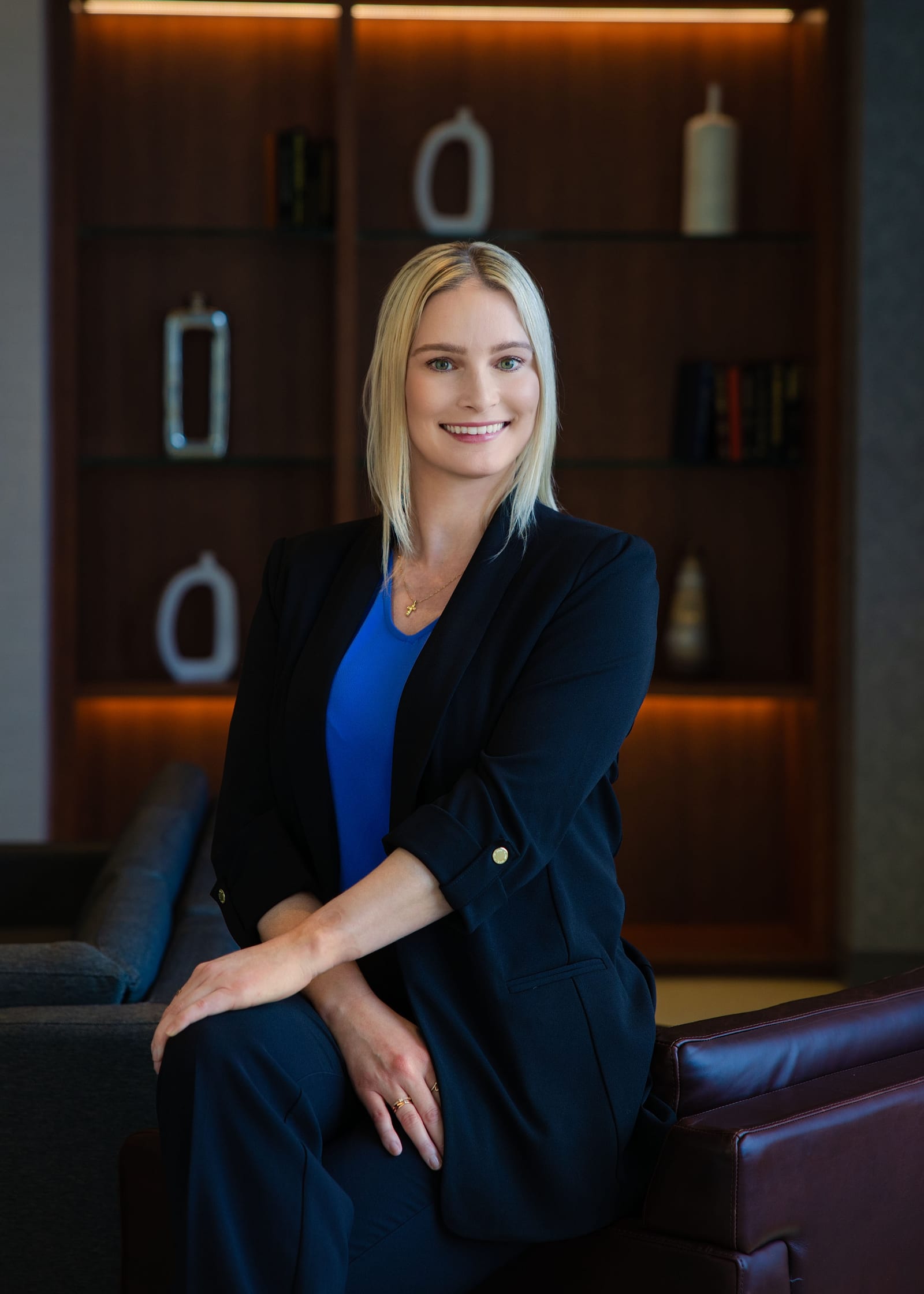 Executive in a navy blazer perched on a leather bench in a warmly lit interior
