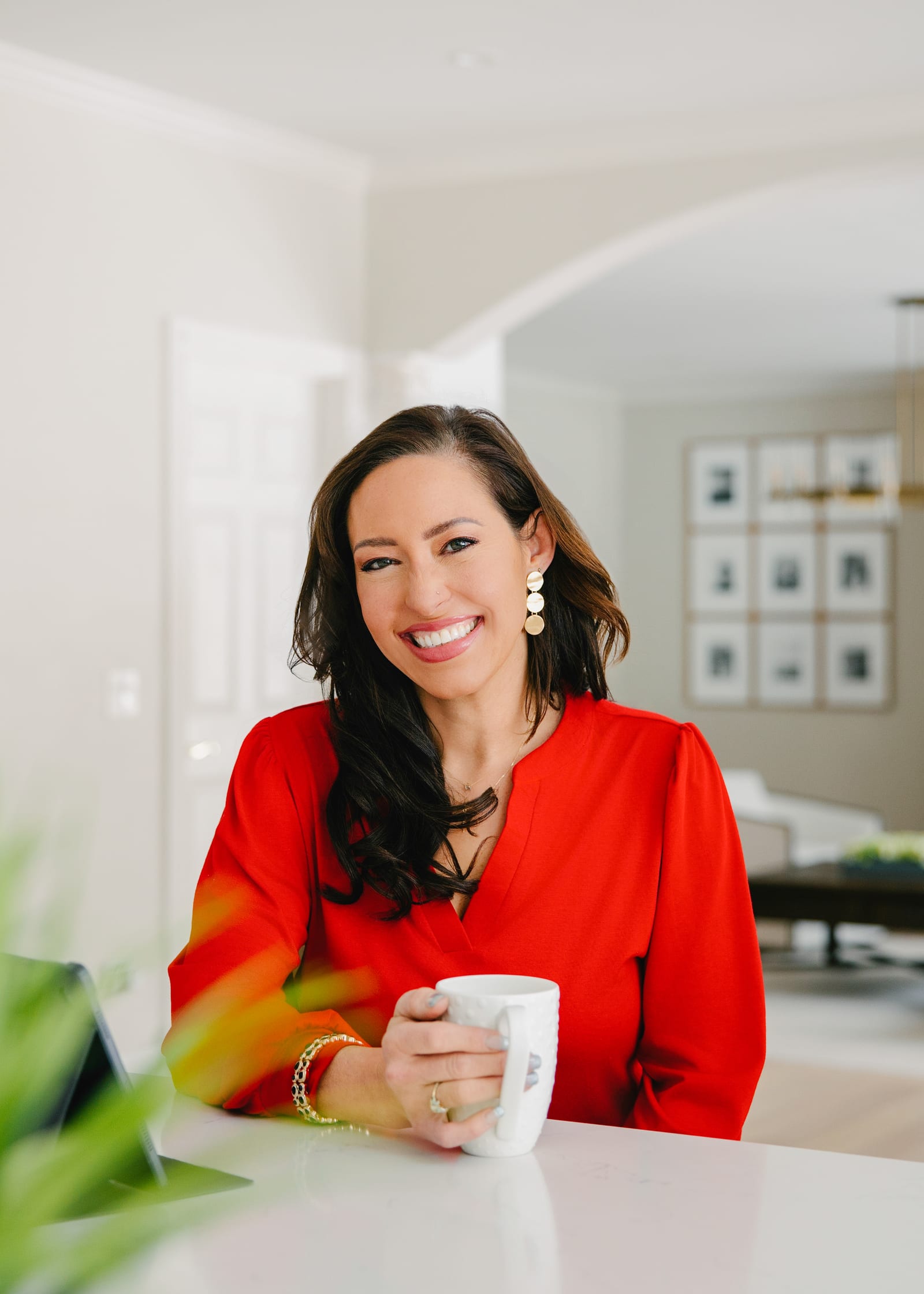 Business owner in a red blazer holding a coffee cup at a bright table beside a window