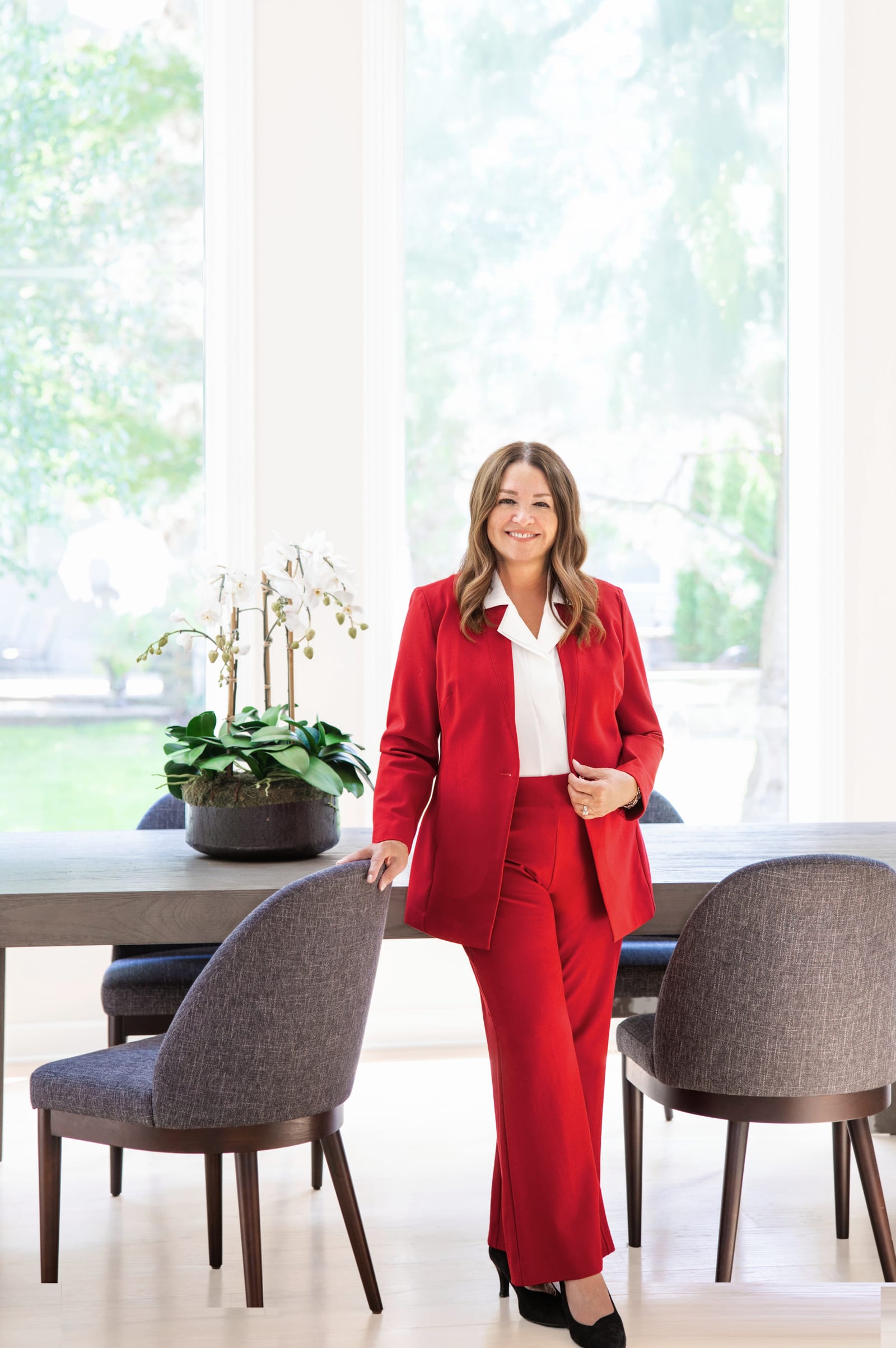 Business owner in a red trouser suit standing in a bright dining room with orchids