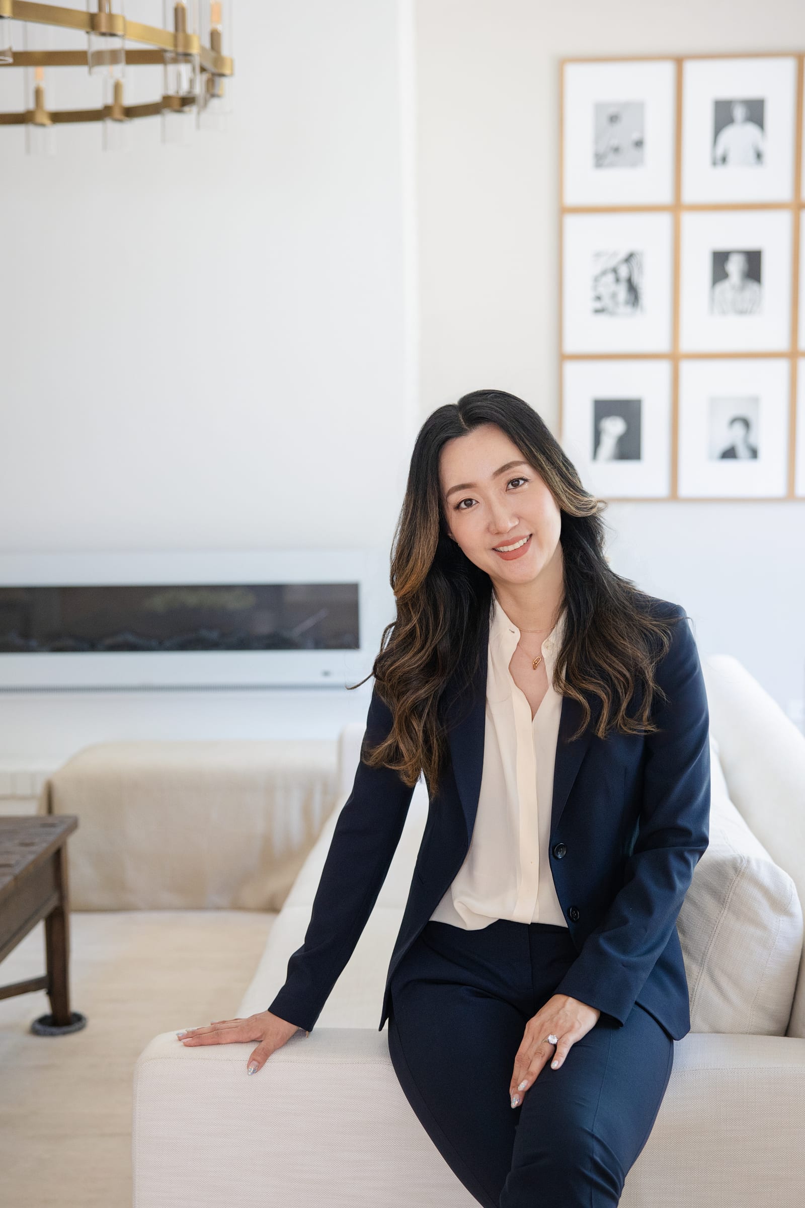 Founder in a navy suit seated on a pale sofa beneath a wall of framed prints