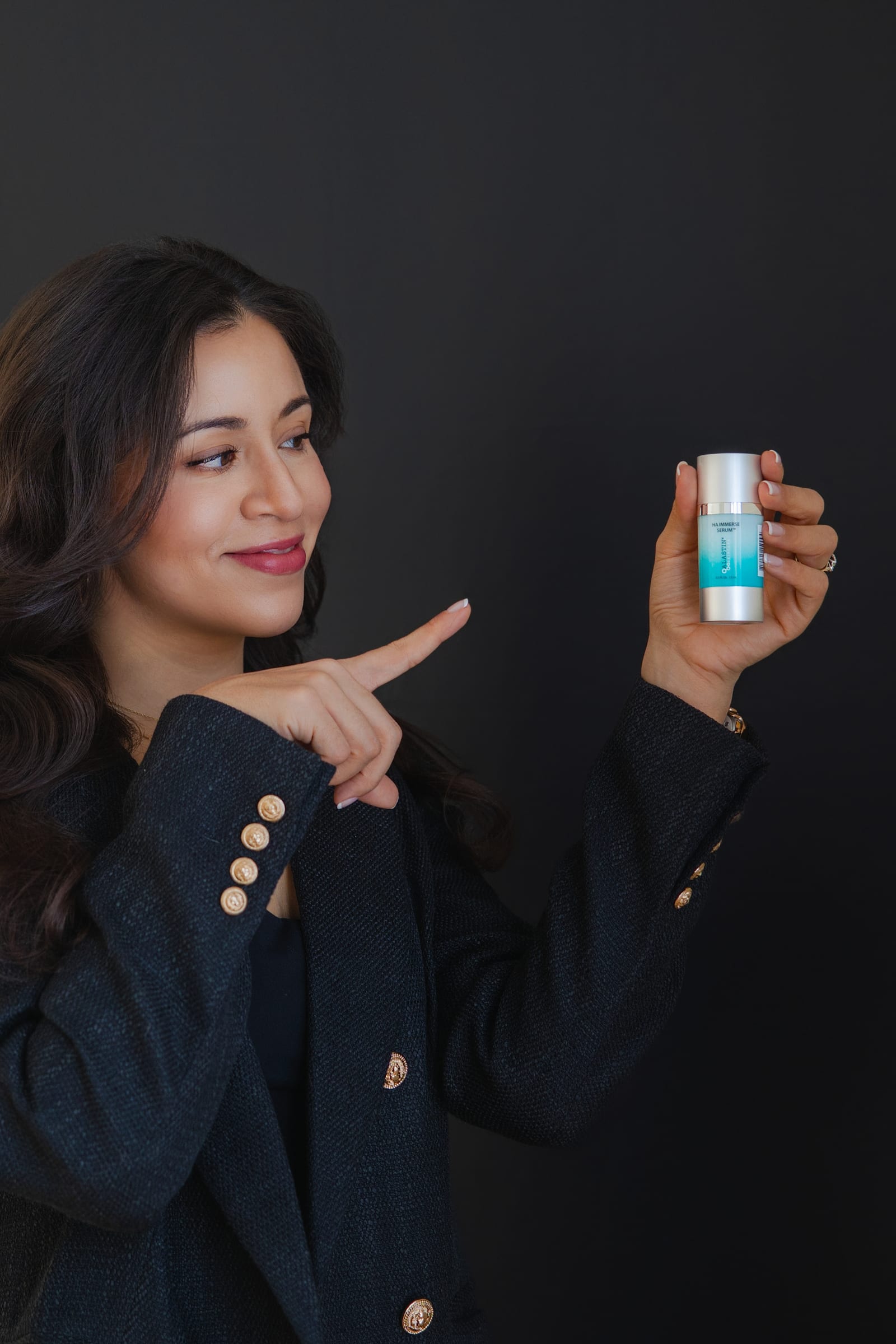 Founder in a navy blazer presenting a small product bottle against a dark ground