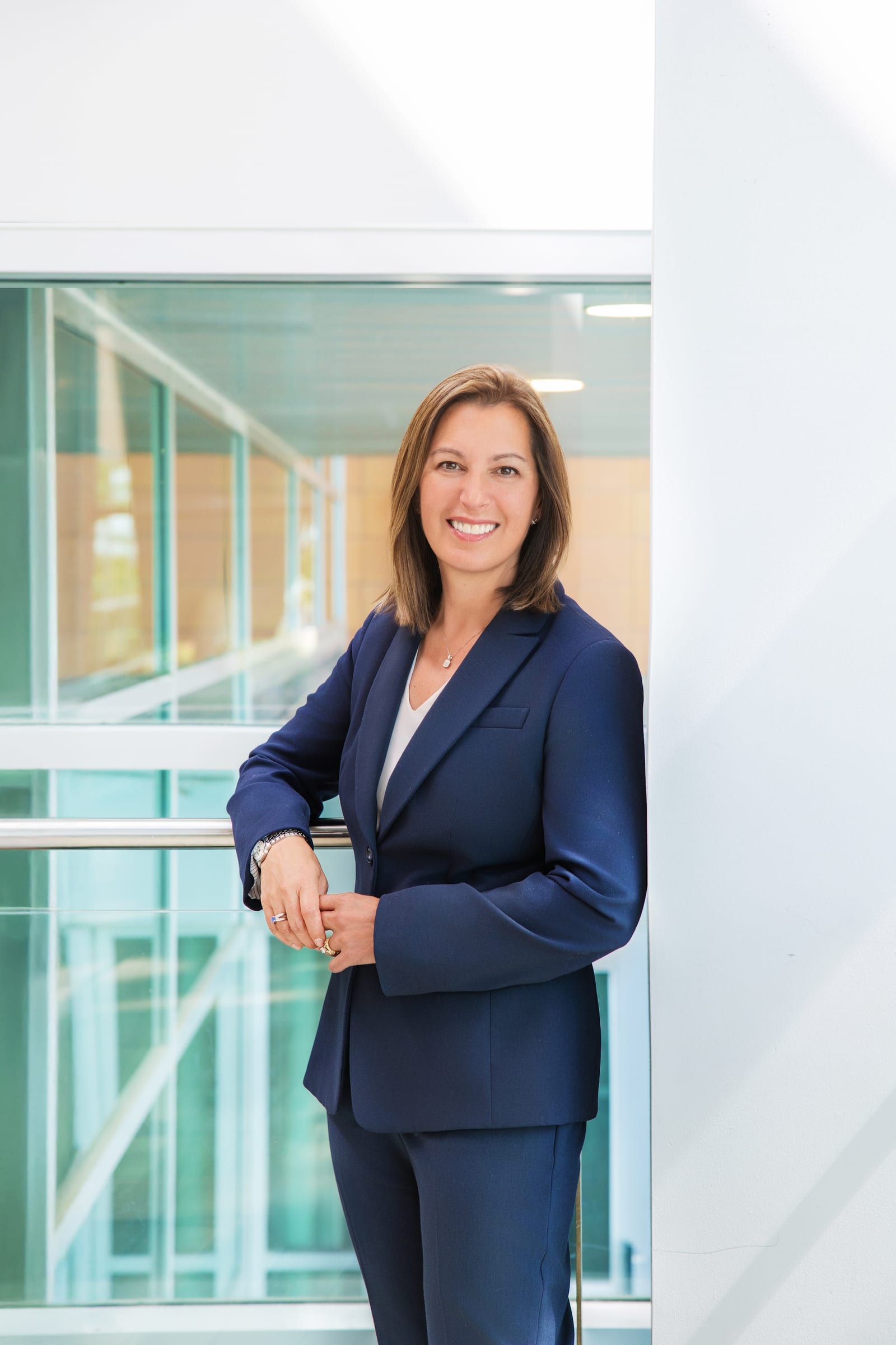 Professional in a navy suit standing beside a bright glass wall