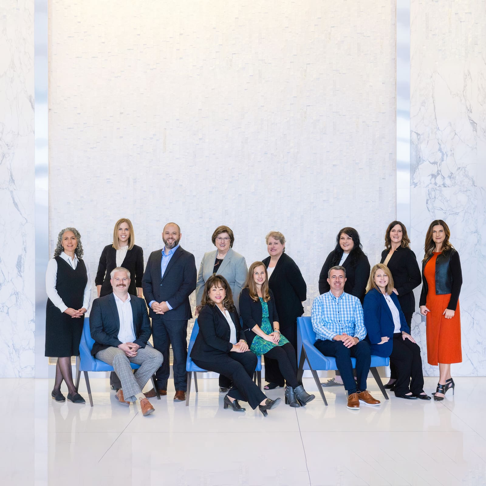 A team of fourteen photographed together, seated and standing, in a bright marble office lobby