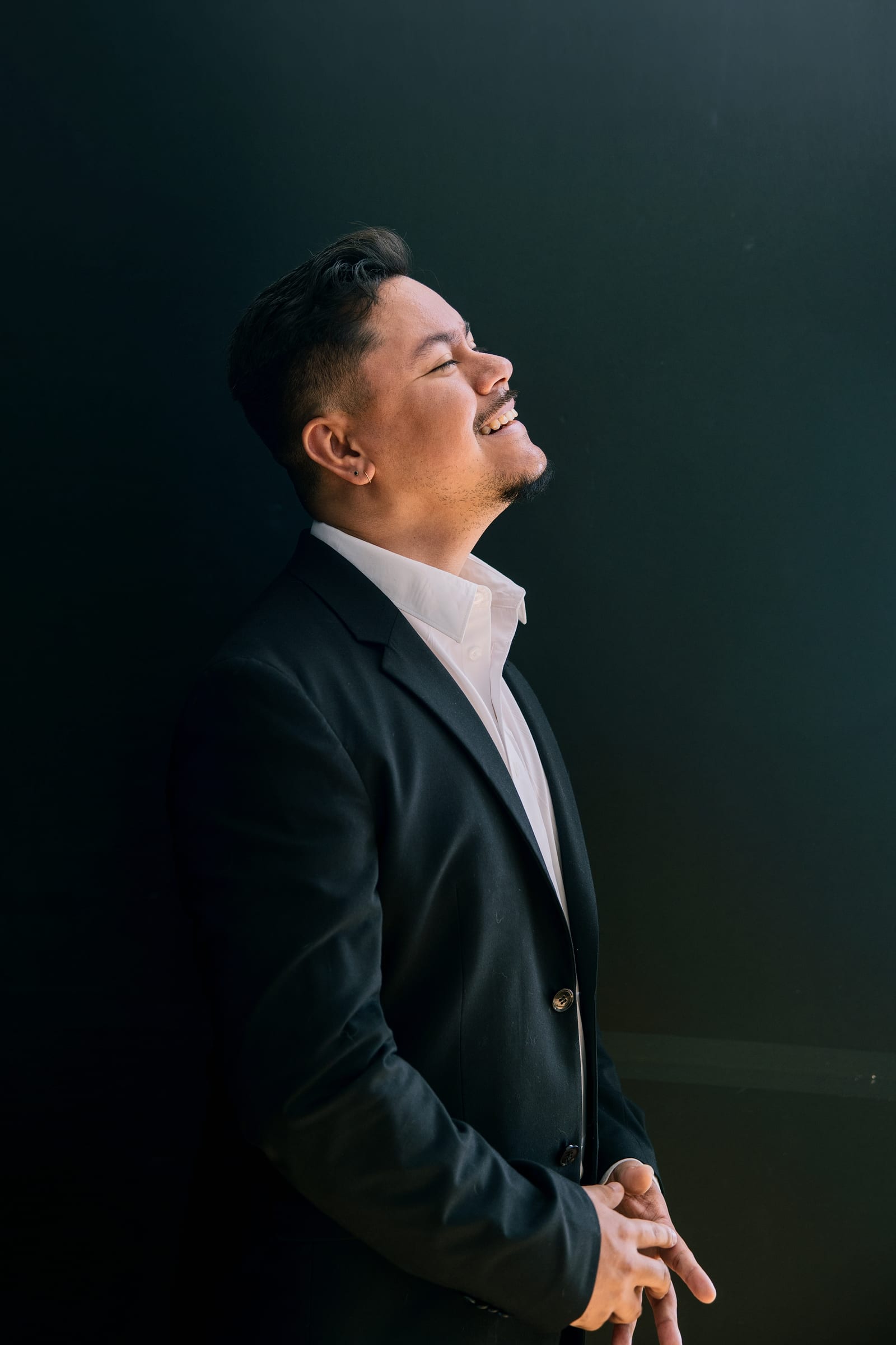 Executive in a dark jacket laughing with head tilted back, lit by a single warm beam against near-black