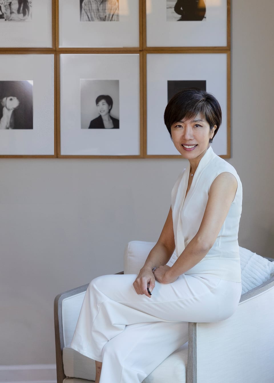 Photographer in white seated on a sofa arm before a wall of framed black-and-white prints