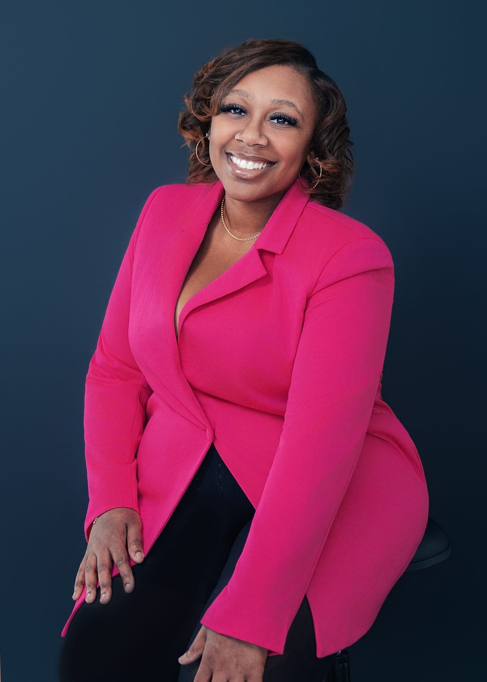 Professional in a magenta blazer seated and laughing against a slate ground