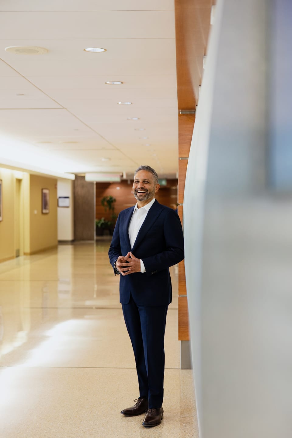 Physician in a blue suit standing in a curved, light-filled hospital corridor
