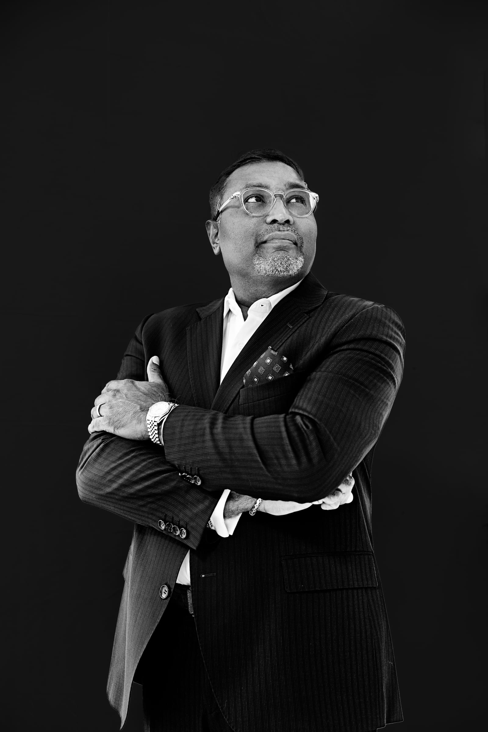 Black and white portrait of an executive in a pinstripe suit, arms crossed, looking up and away