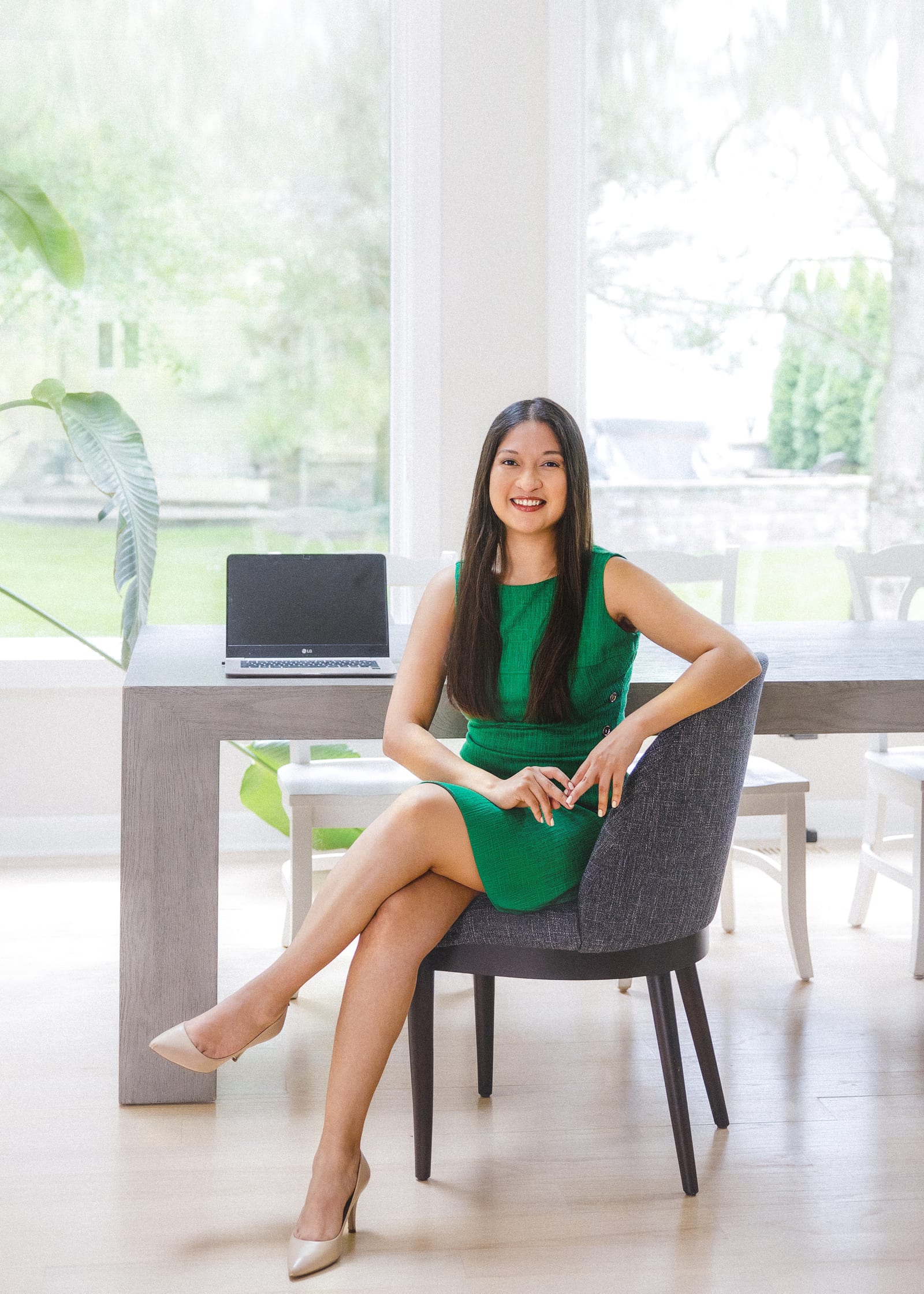 Business owner in a green dress seated at a desk in front of a wide garden window
