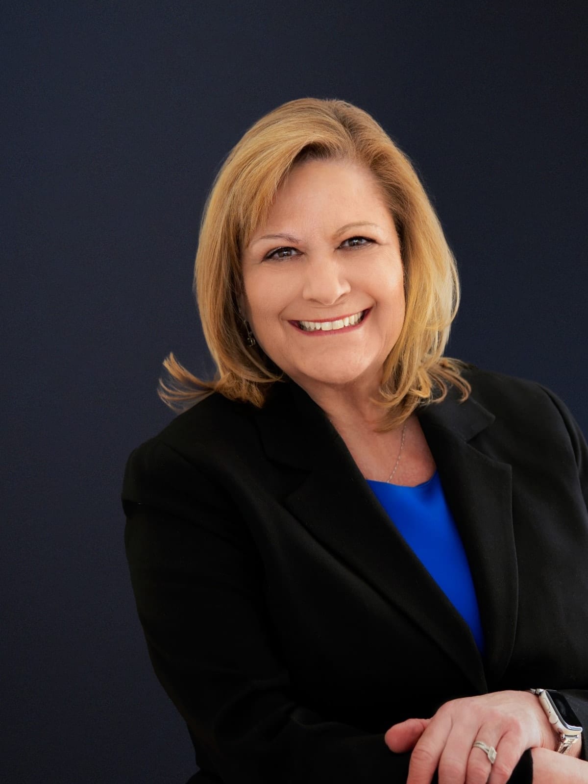 Executive in a black blazer over a cobalt dress, seated, against a deep navy ground