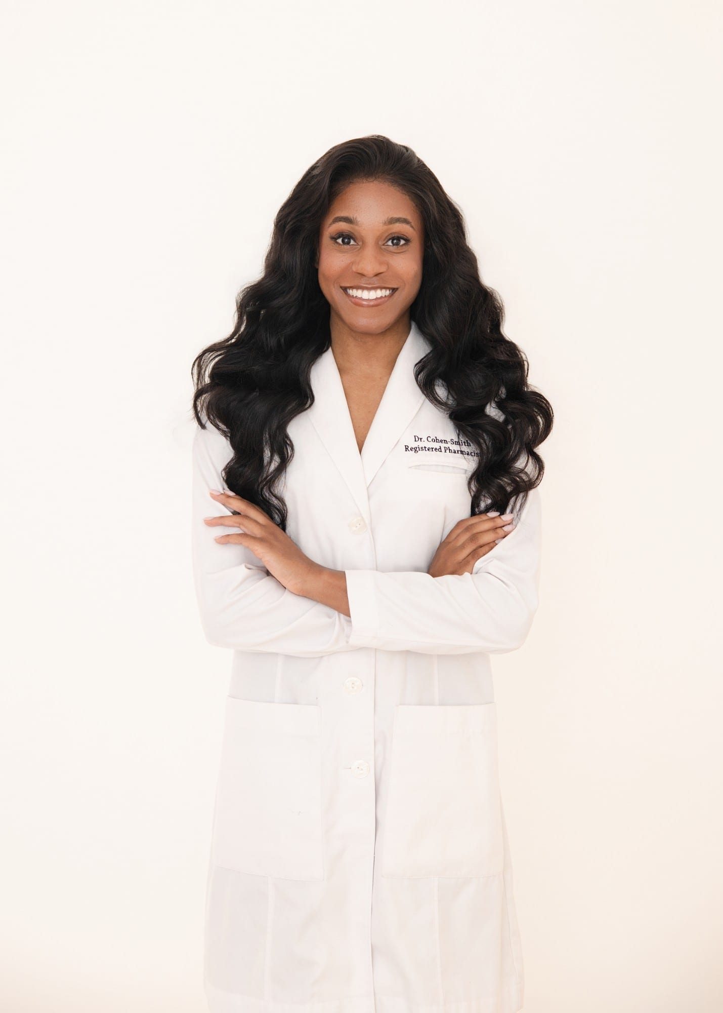 Pharmacist in a white coat with arms folded, against a warm white ground