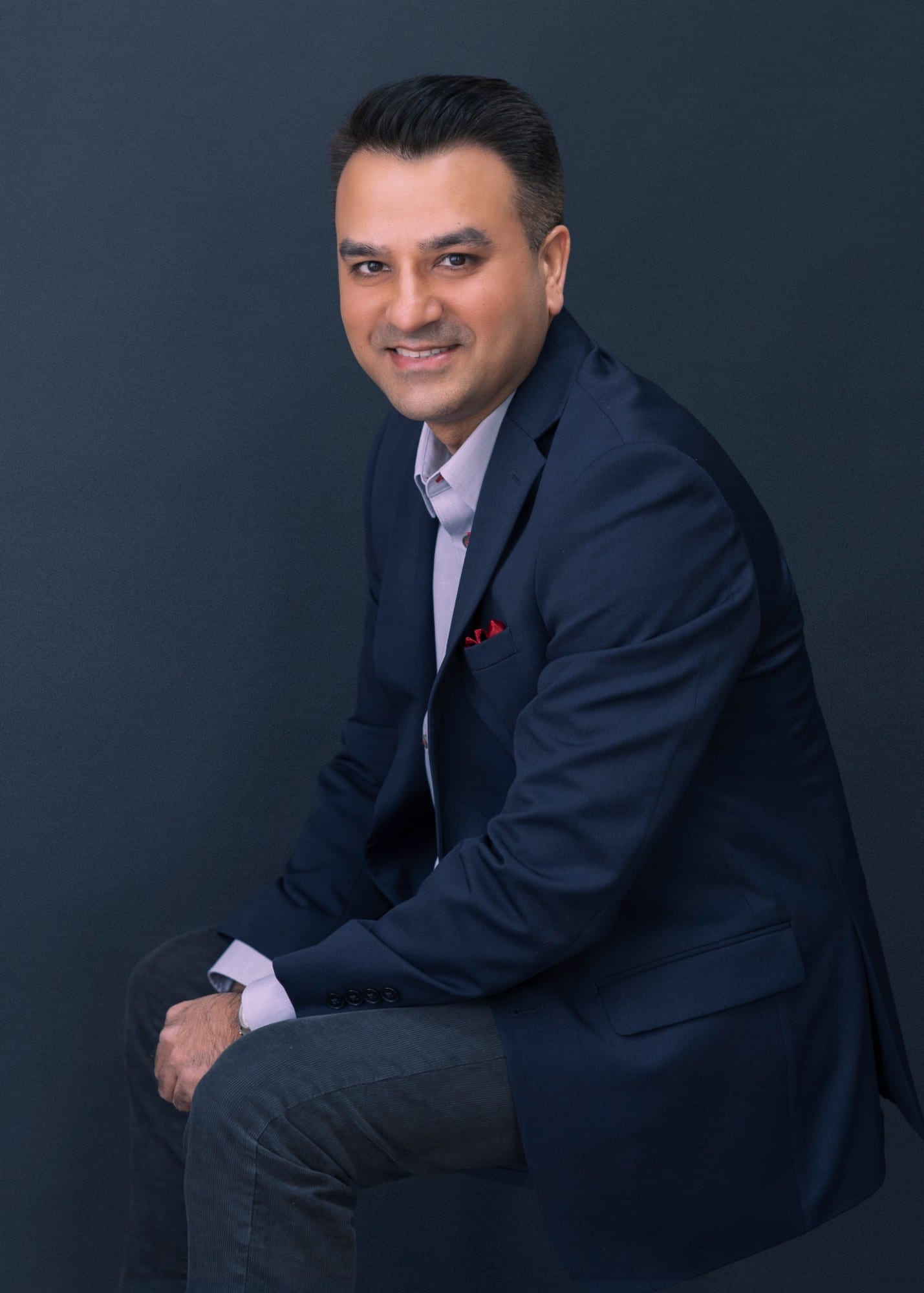 Professional in a navy blazer seated and turned to camera, against a deep navy ground