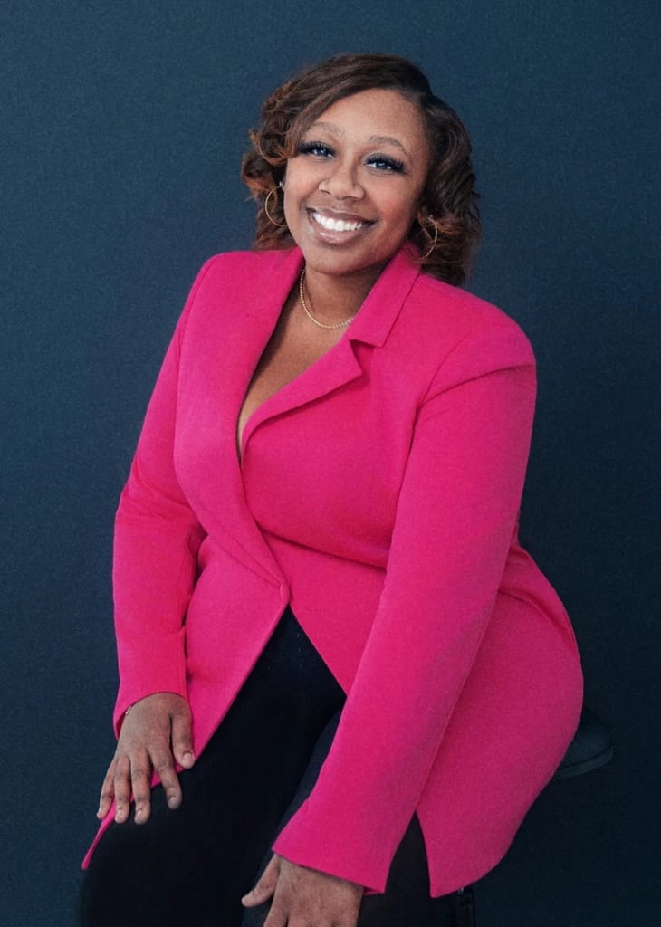 Professional in a pink blazer seated, leaning in, against a deep navy ground