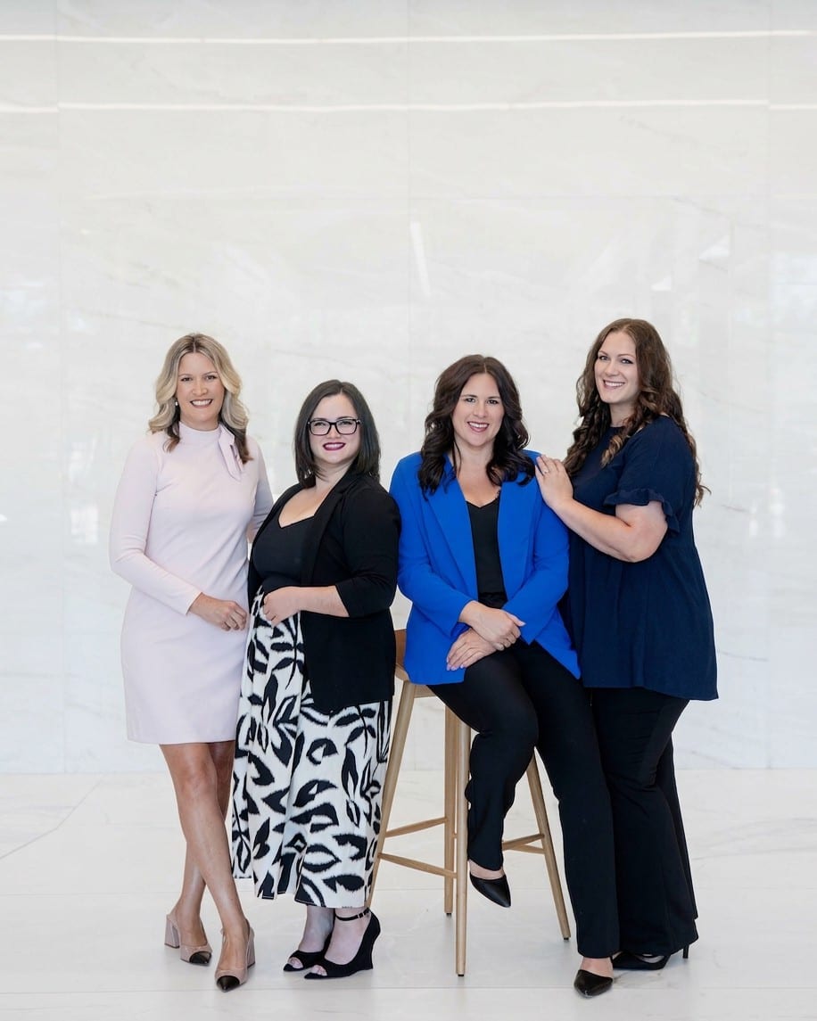 Four women from one firm in a bright marble lobby, one seated on a stool