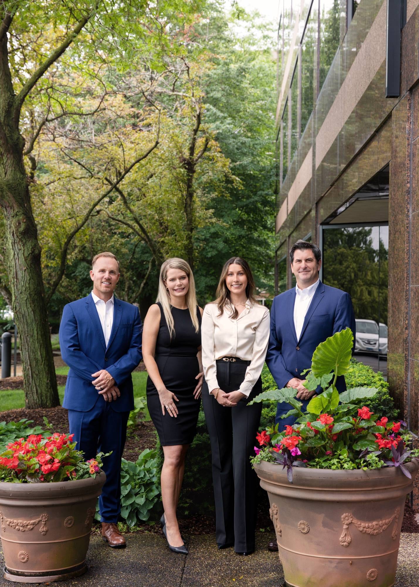 Four colleagues outside their office building among planters of red begonias